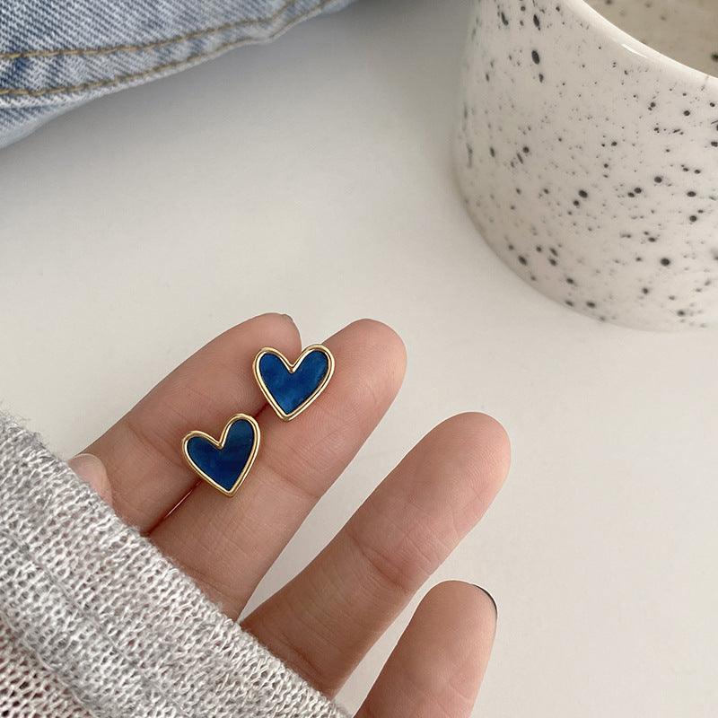 Blue heart earrings in models hand with white background