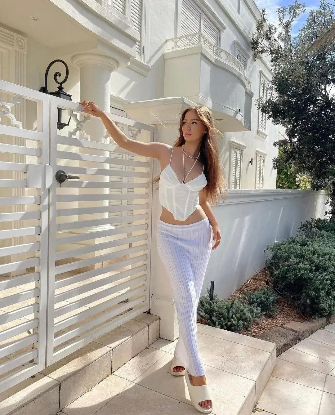 Woman wearing a ribbed bodycon maxi skirt stands near a white fence in a bright, sunny outdoor setting.