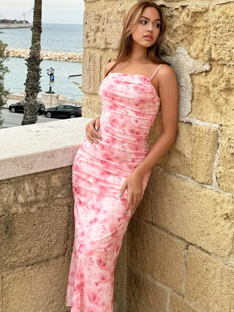 Model wearing pink floral maxi dress stone wall sea in background