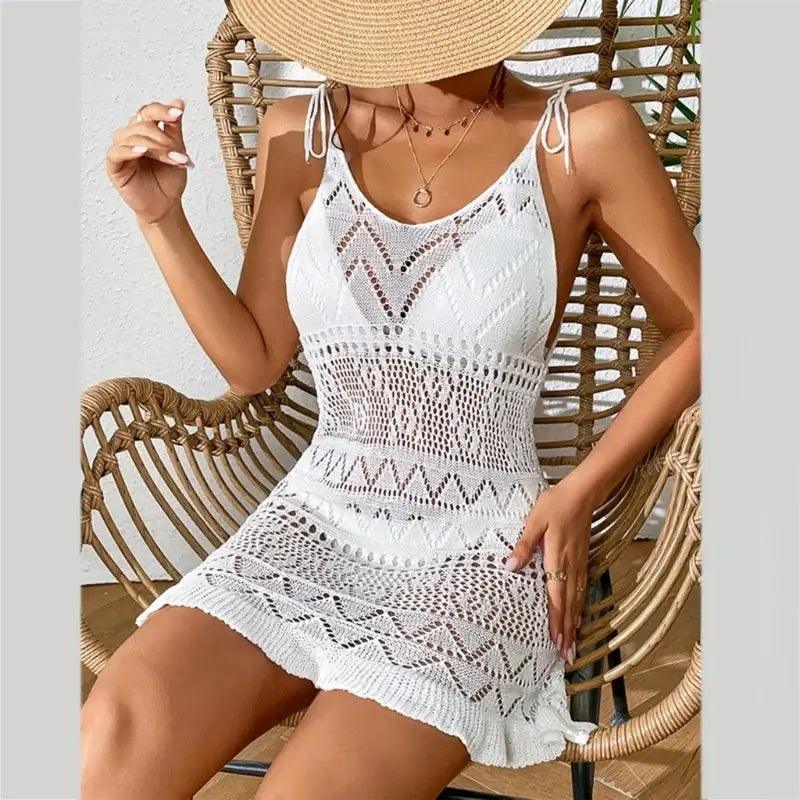 Model sat down wearing white see through crochet dress and white bikini with a sun hat