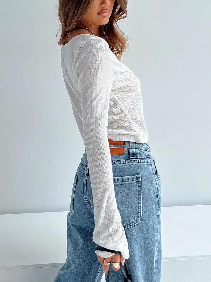 Woman posing wearing white cardigan and blue jeans holding handbag