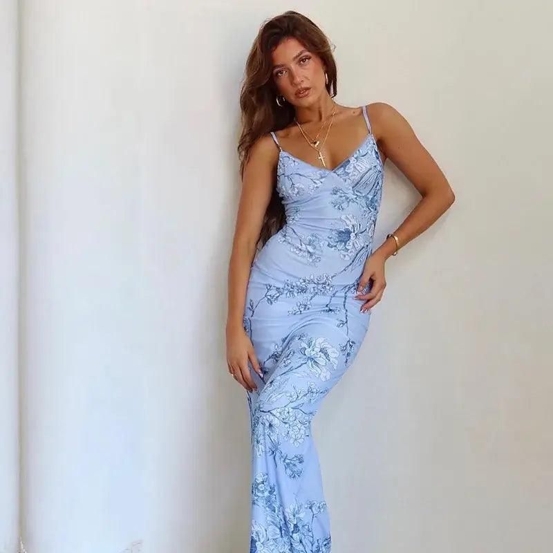 Woman wearing blue floral bodycon thin strap evening maxi dress against white wall.