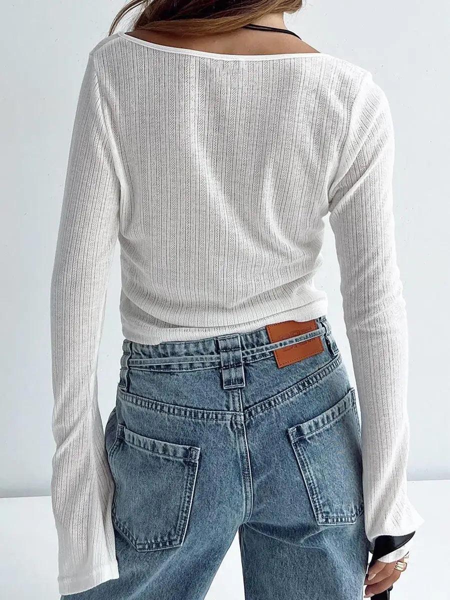 Woman showing back of white long sleeve top with a plain background